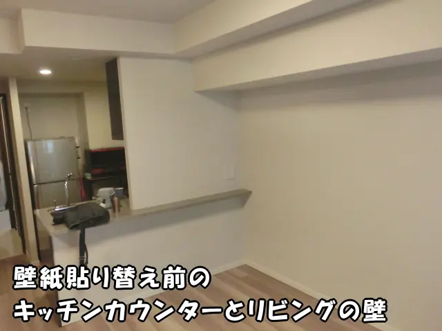 壁紙貼り替え前のキッチンカウンターとリビングの壁の様子。無地の白い壁紙で仕上げられ、個性がありません。